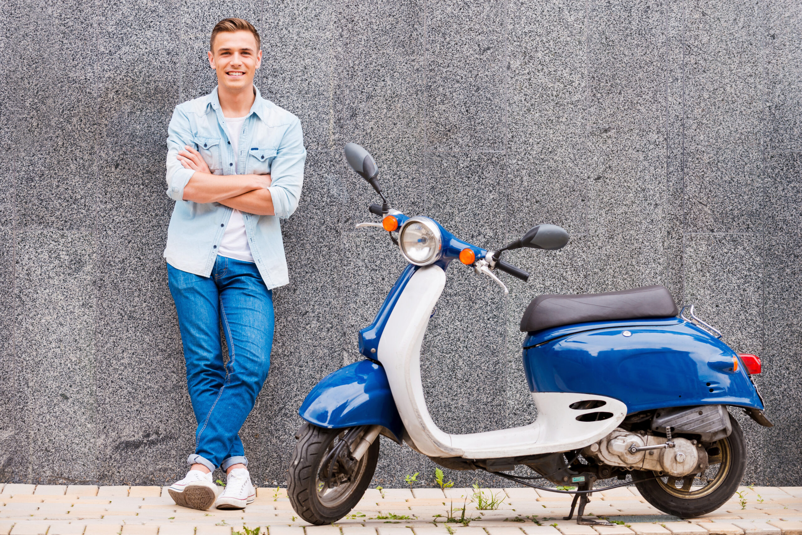 Me and my new scooter. Handsome young man leaning at the wall and smiling while standing near his new scooter